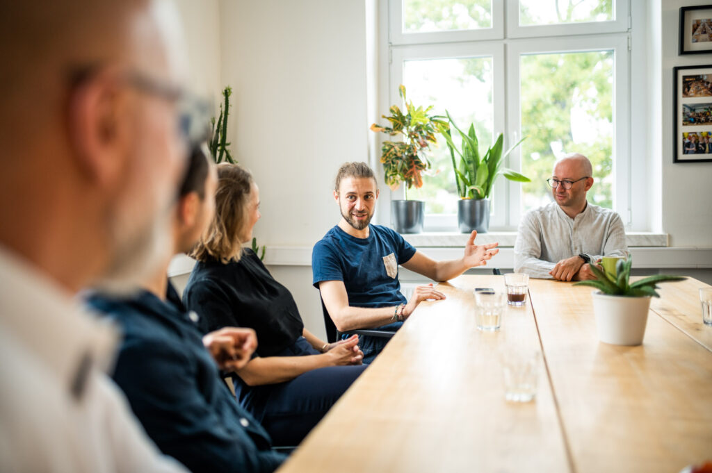 Workshop Situation, mehrere Personen sitzen um einen Tisch und diskutieren
